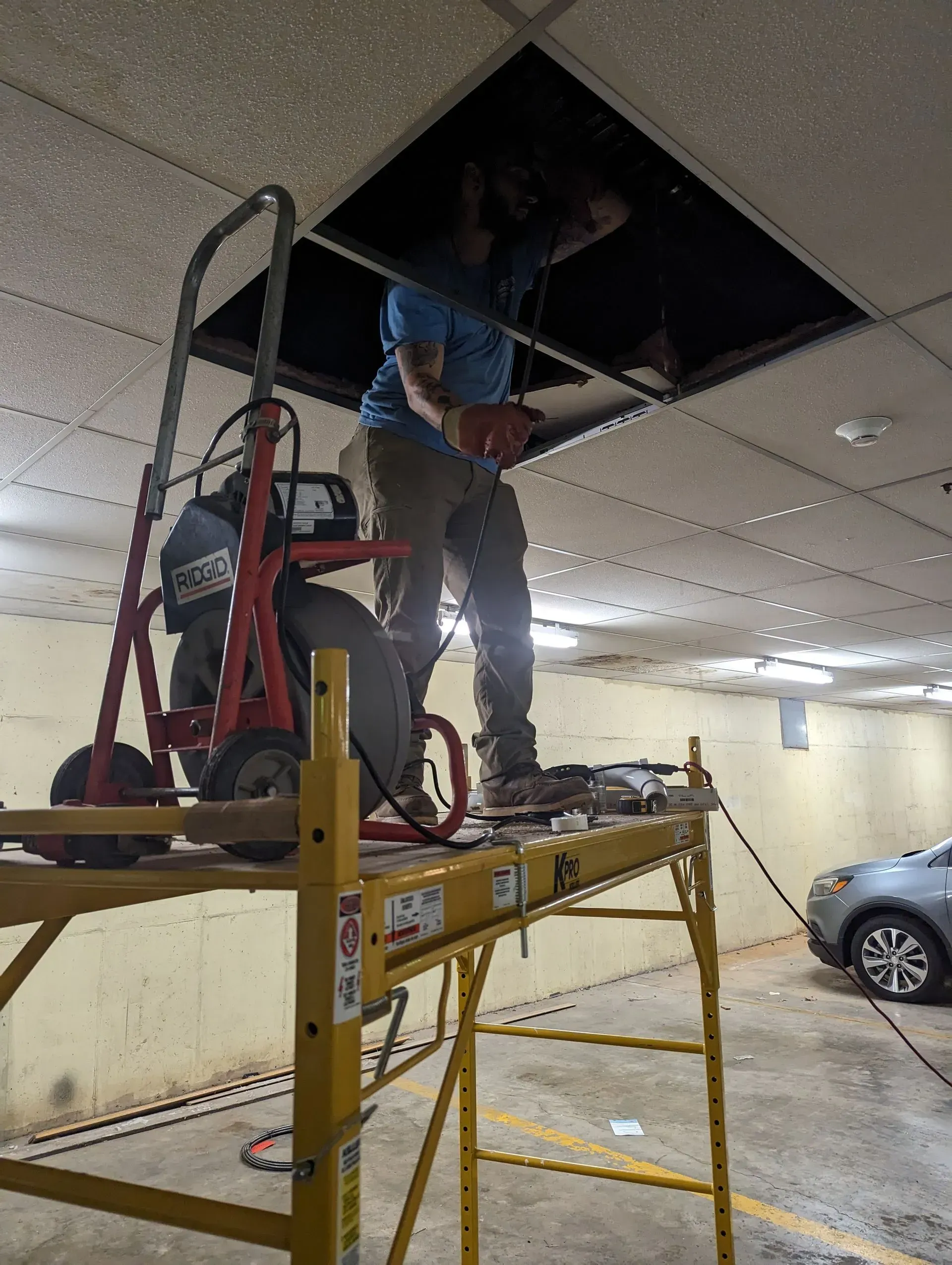 A man is standing on a scaffolding looking into a hole in the ceiling.