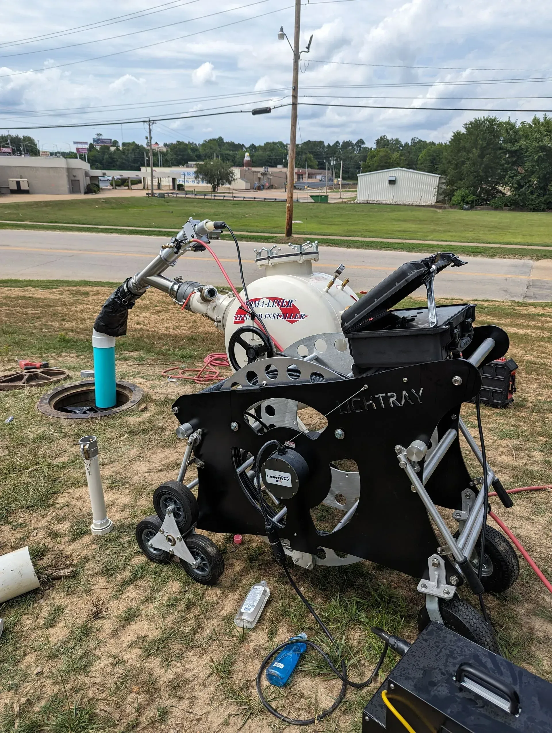 A robot is sitting in the grass next to a manhole cover.