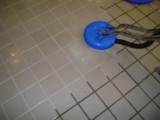 A cleaning tool deep cleans a section of light-colored tile flooring, revealing a stark contrast against dirty grout.