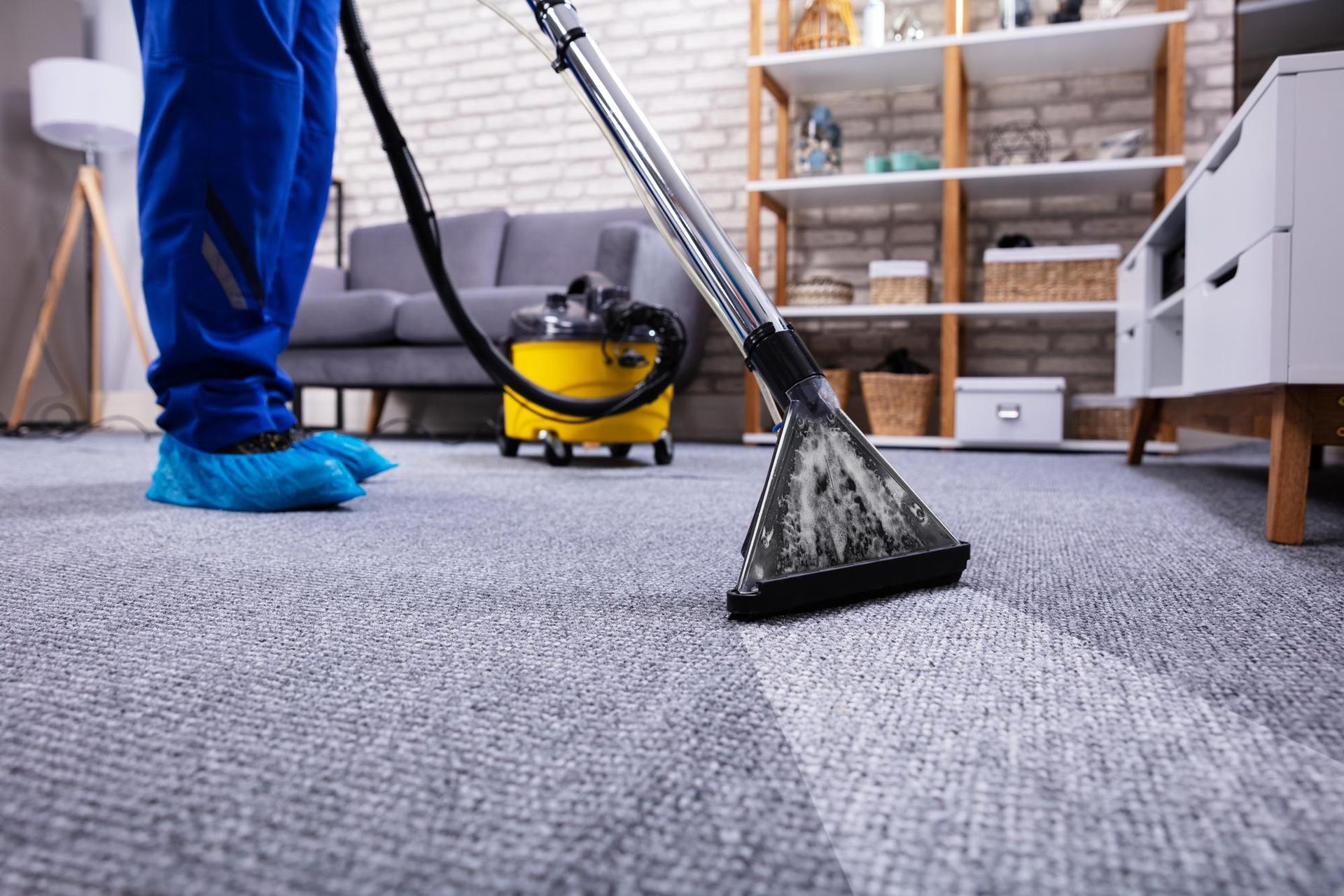 Three blue industrial fans dry a beige carpet in a living room near a fireplace.