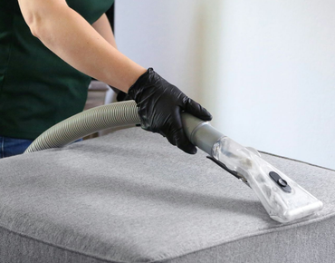 A vacuum cleaner nozzle cleaning a beige upholstered sofa cushion.