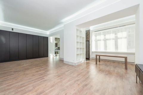 A bright, minimalist room featuring dark wood-paneled walls, light wood flooring, a white shelf unit, and a wooden table.
