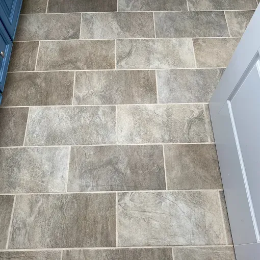 A close-up of a gray-toned, stone-look tile floor with a running bond pattern, next to blue and gray cabinets.