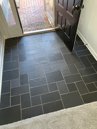A front entryway featuring a charcoal grey tiled floor in a pattern, leading to an open door onto a brick porch.