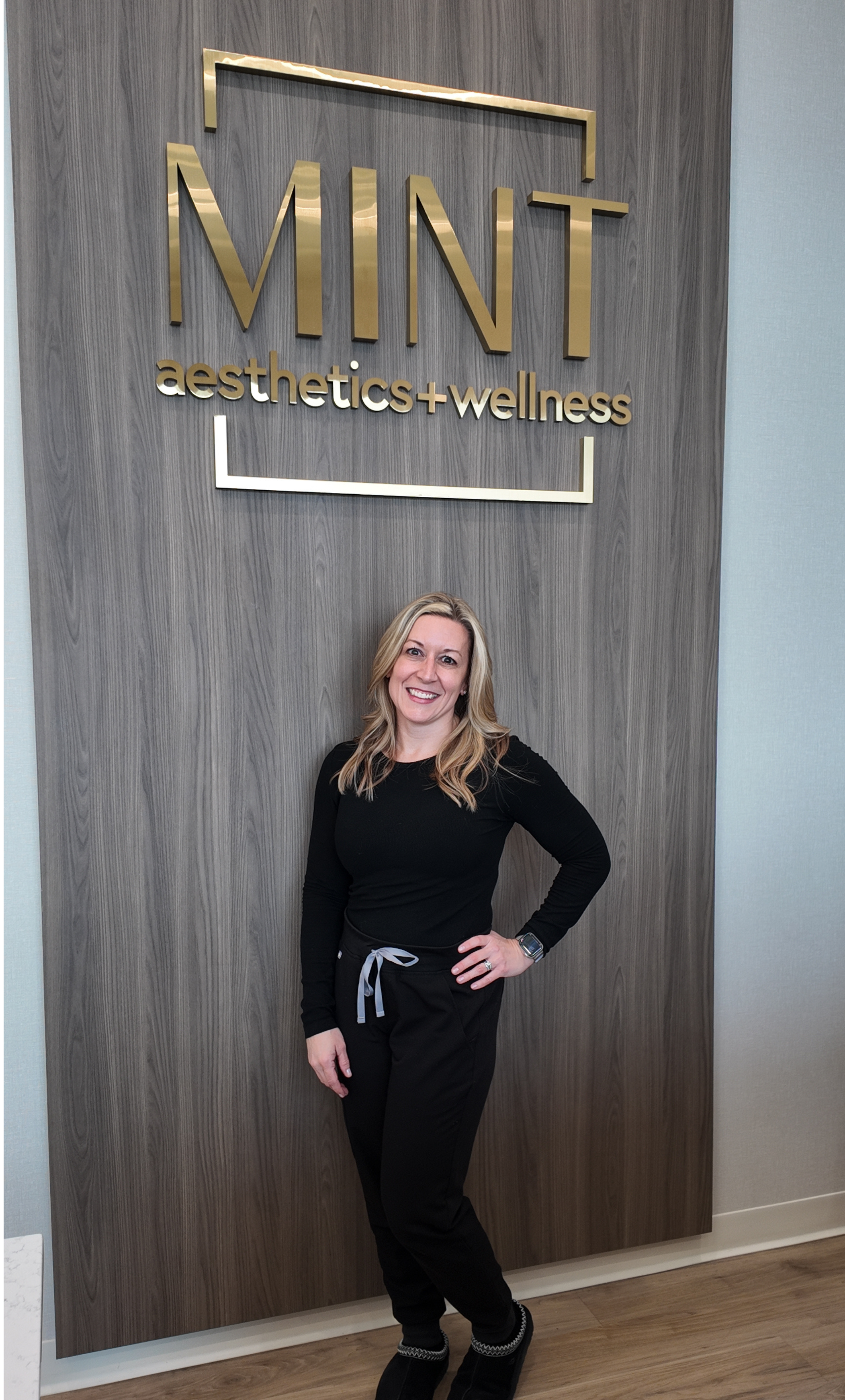 A woman in a black turtleneck is smiling for the camera while standing on a porch.