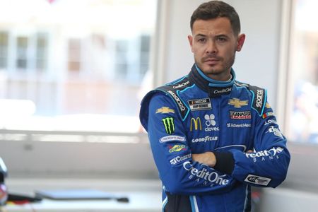 Kyle Larson standing in a garage with his arms crossed.