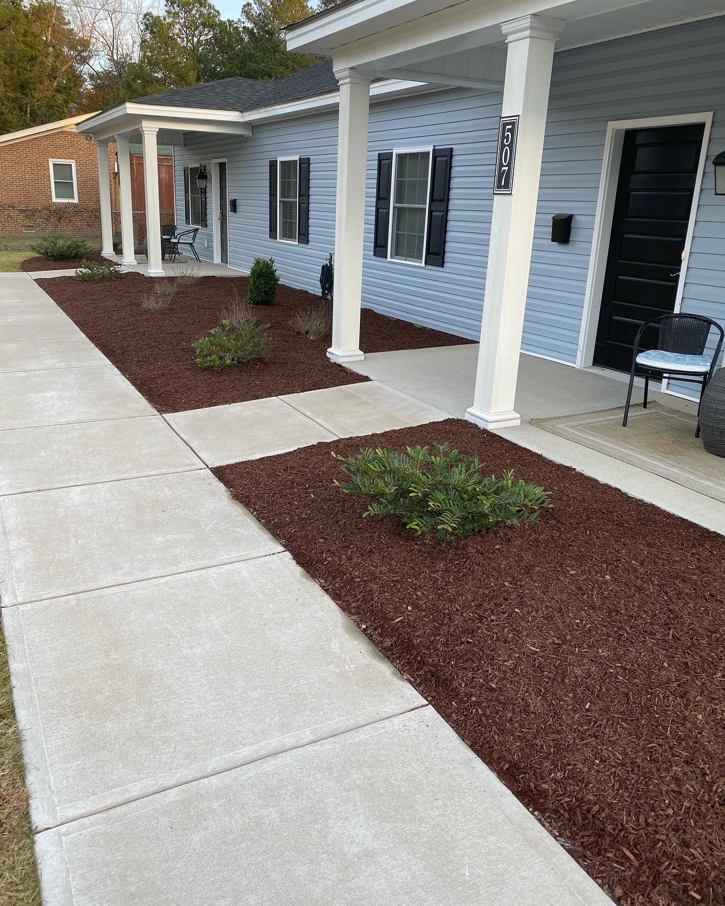 A concrete walkway leading to a blue house with a porch.