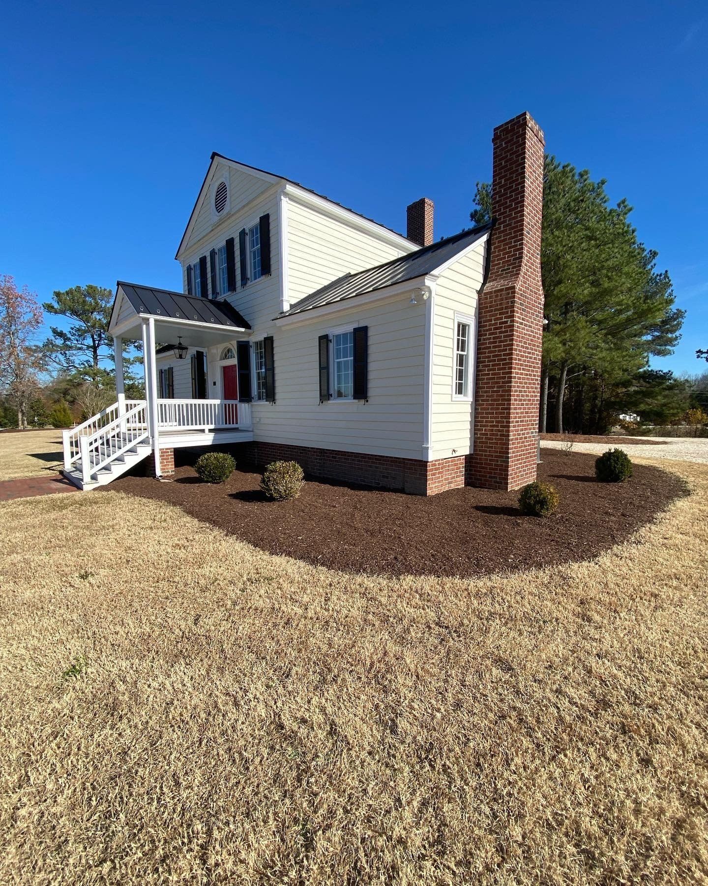 A large white house with a brick chimney is sitting in the middle of a field.