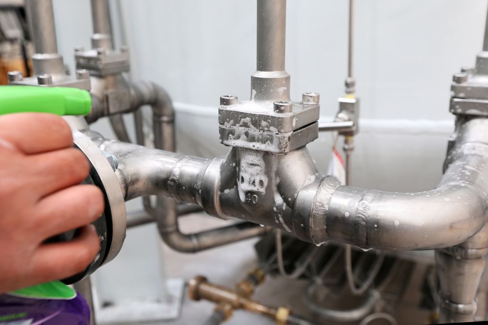 A Person Is Cleaning A Stainless Steel Pipe With A Spray Bottle — H2O Plumbing & Maintenance Services In Armidale, NSW