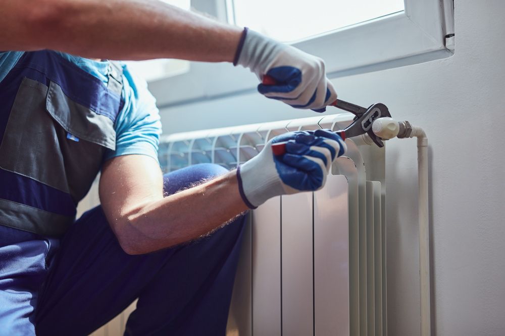 A Man Is Fixing A Radiator With A Wrench — H2O Plumbing & Maintenance Services In Armidale, NSW