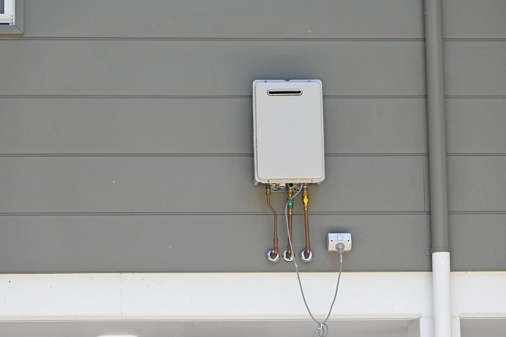 A White Water Heater Is Attached To The Side Of A House — H2O Plumbing & Maintenance Services In Armidale, NSW
