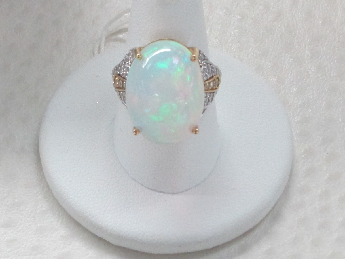 Oval opal ring with diamond accents on a white display stand.