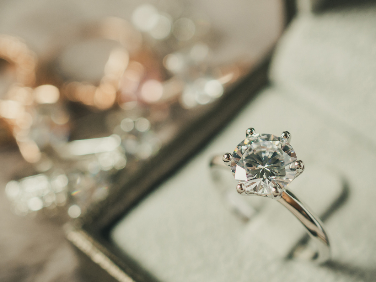 Diamond engagement ring in a ring box, other jewelry blurred in background.