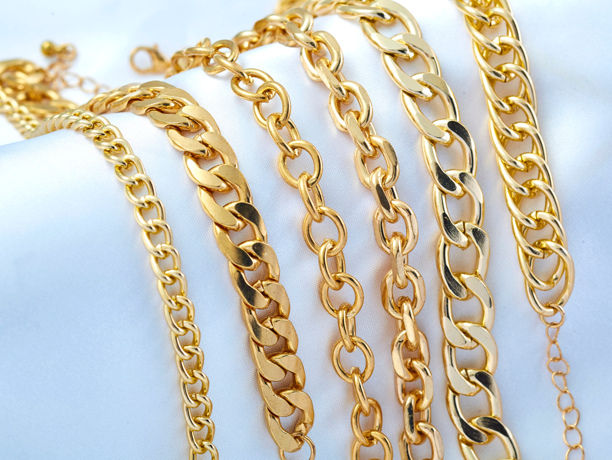 Gold chain bracelets of various sizes on a white cloth.