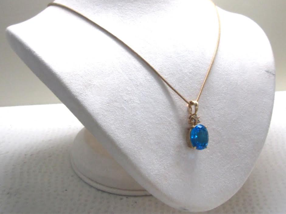 Gold necklace with a blue gemstone pendant on a white jewelry display.