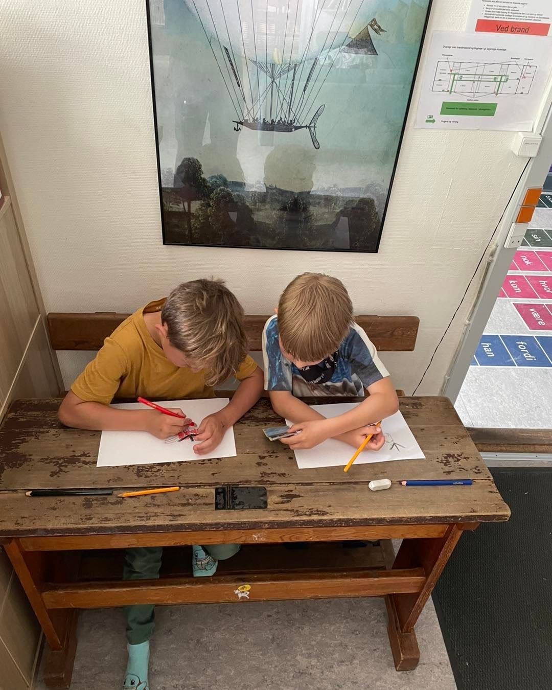 To unge drenge sidder ved et træbord og skriver på et stykke papir.