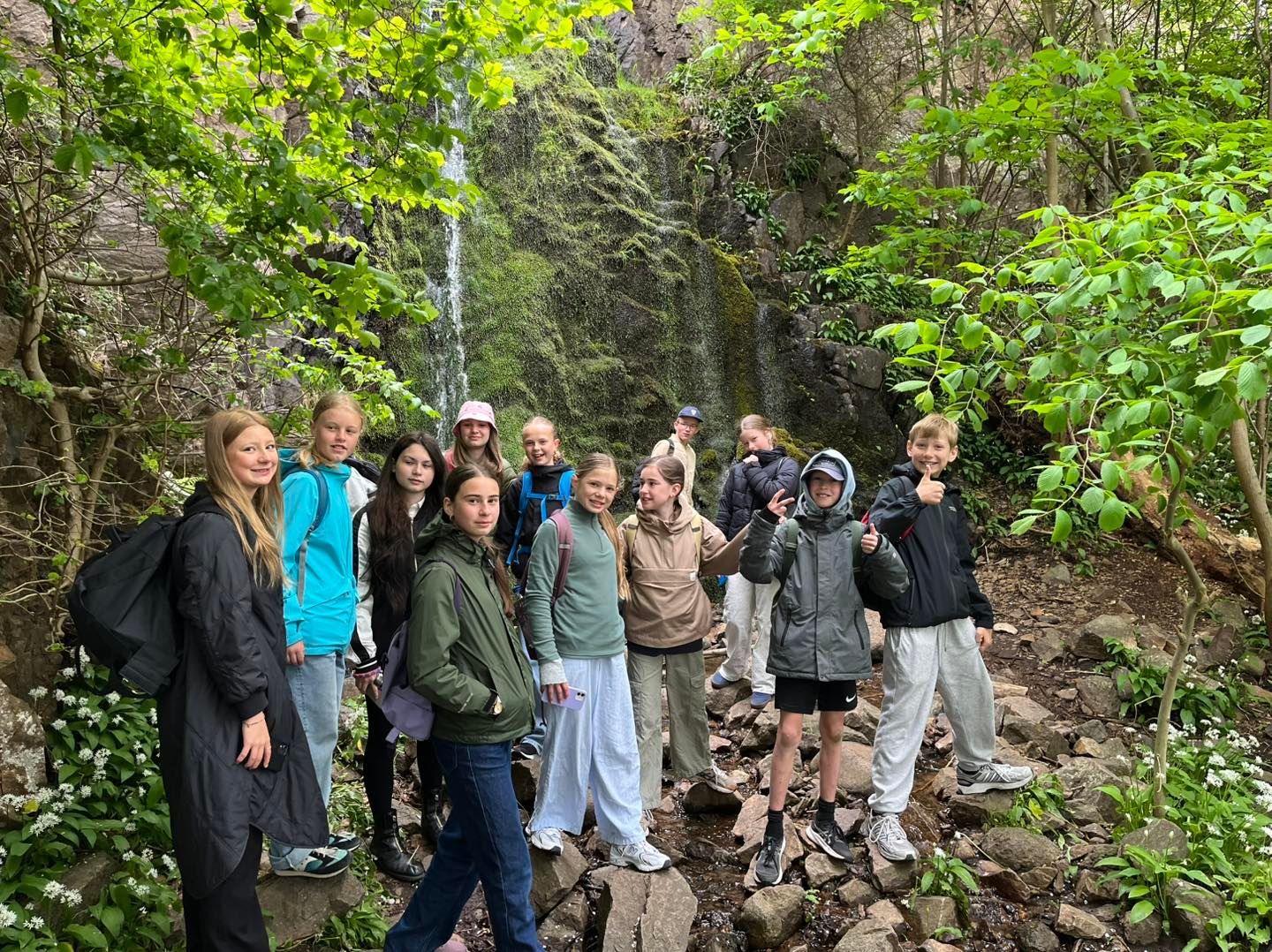En gruppe unge mennesker står på en stenet sti i skoven.