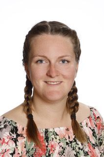 En kvinde med fletninger har en blomstret kjole på og smiler.