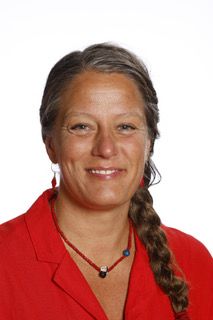 En kvinde i en rød jakke og halskæde smiler til kameraet.