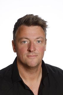 En mand i en sort skjorte står foran en hvid baggrund.