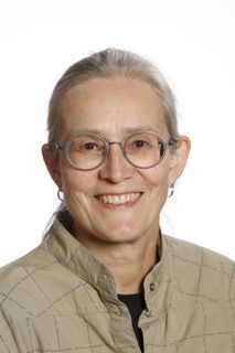 En kvinde med briller og jakke smiler til kameraet.