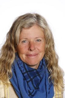 En kvinde har et blåt tørklæde om halsen og smiler.