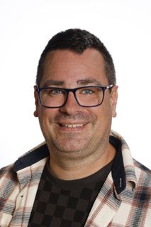 En mand med briller og en ternet skjorte smiler til kameraet.