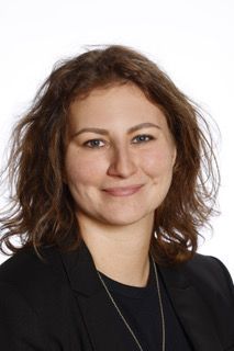 En kvinde iført en sort jakke og en halskæde smiler til kameraet.