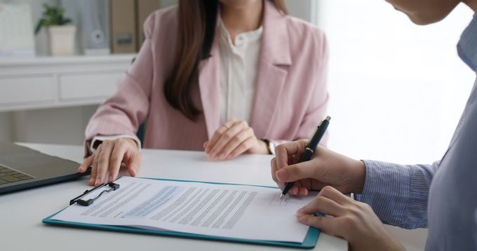 A Woman In A Pink Jacket Holding A Document While Someone Else Signs It — Pollock Ingram Solicitors in Caloundra, QLD
