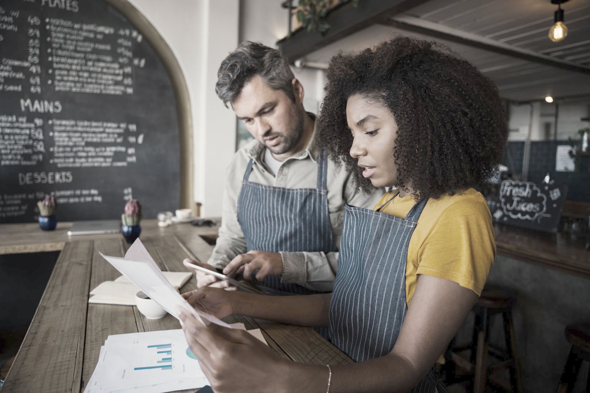 A man and a woman are sitting at a table in a restaurant looking at papers.