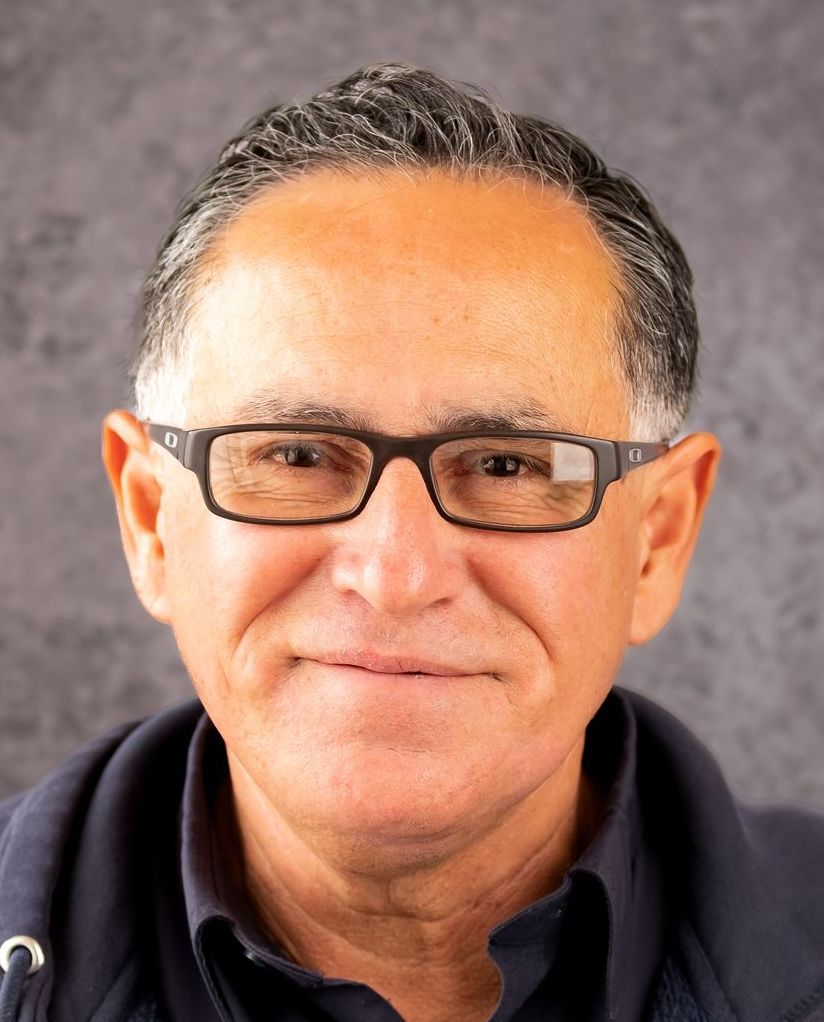 A man wearing glasses and a blue shirt is smiling for the camera.