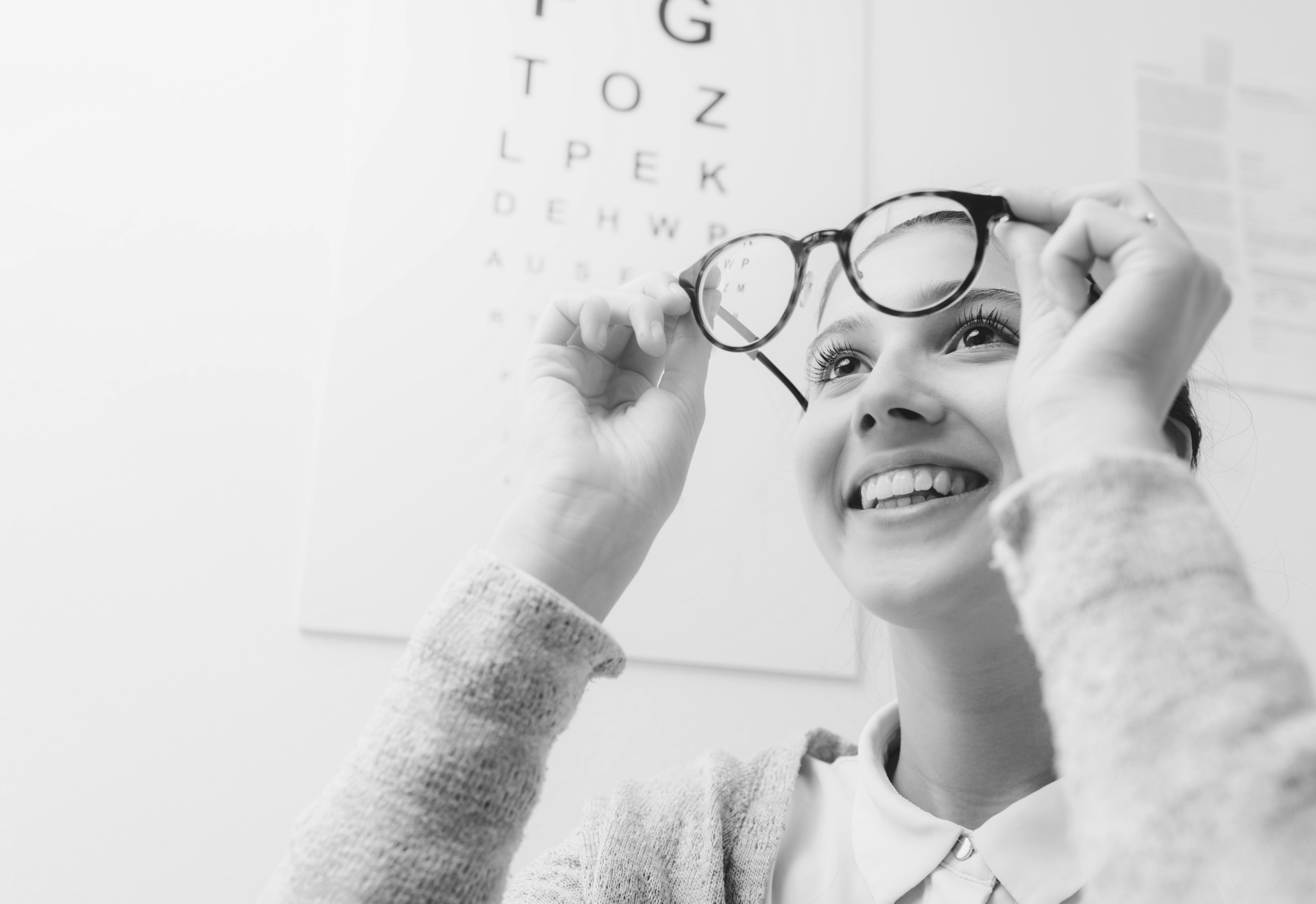 a woman adjusts her glasses in front of an eye chart