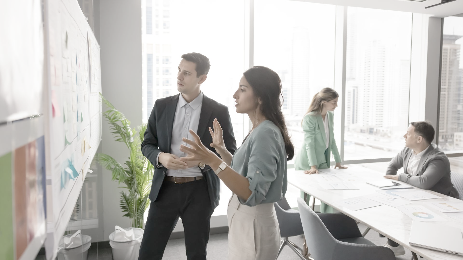 People in business attire discussing charts on a wall in a modern office.
