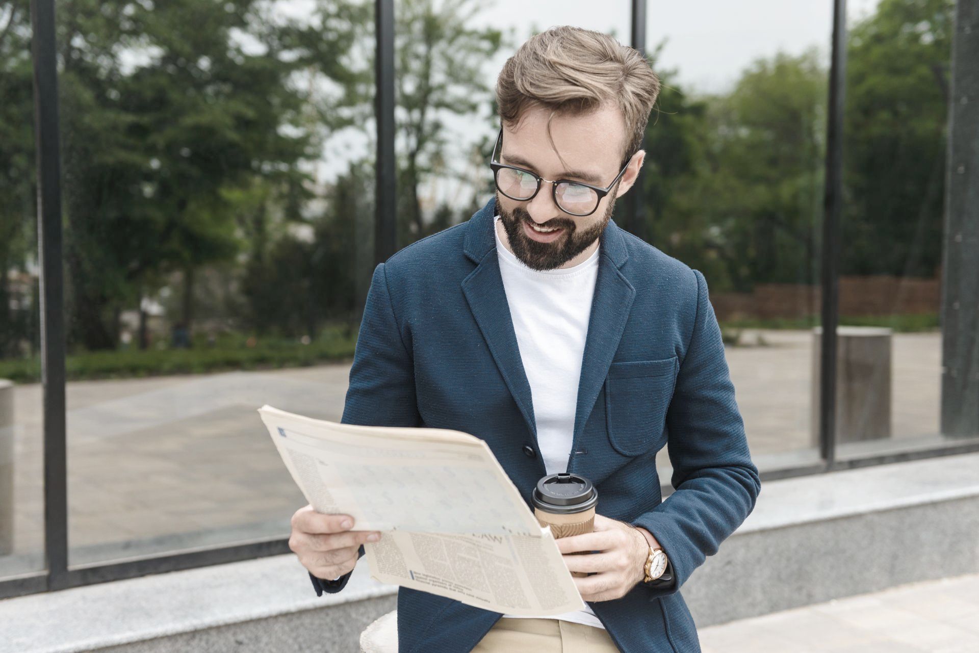 A man is reading a newspaper while holding a cup of coffee.
