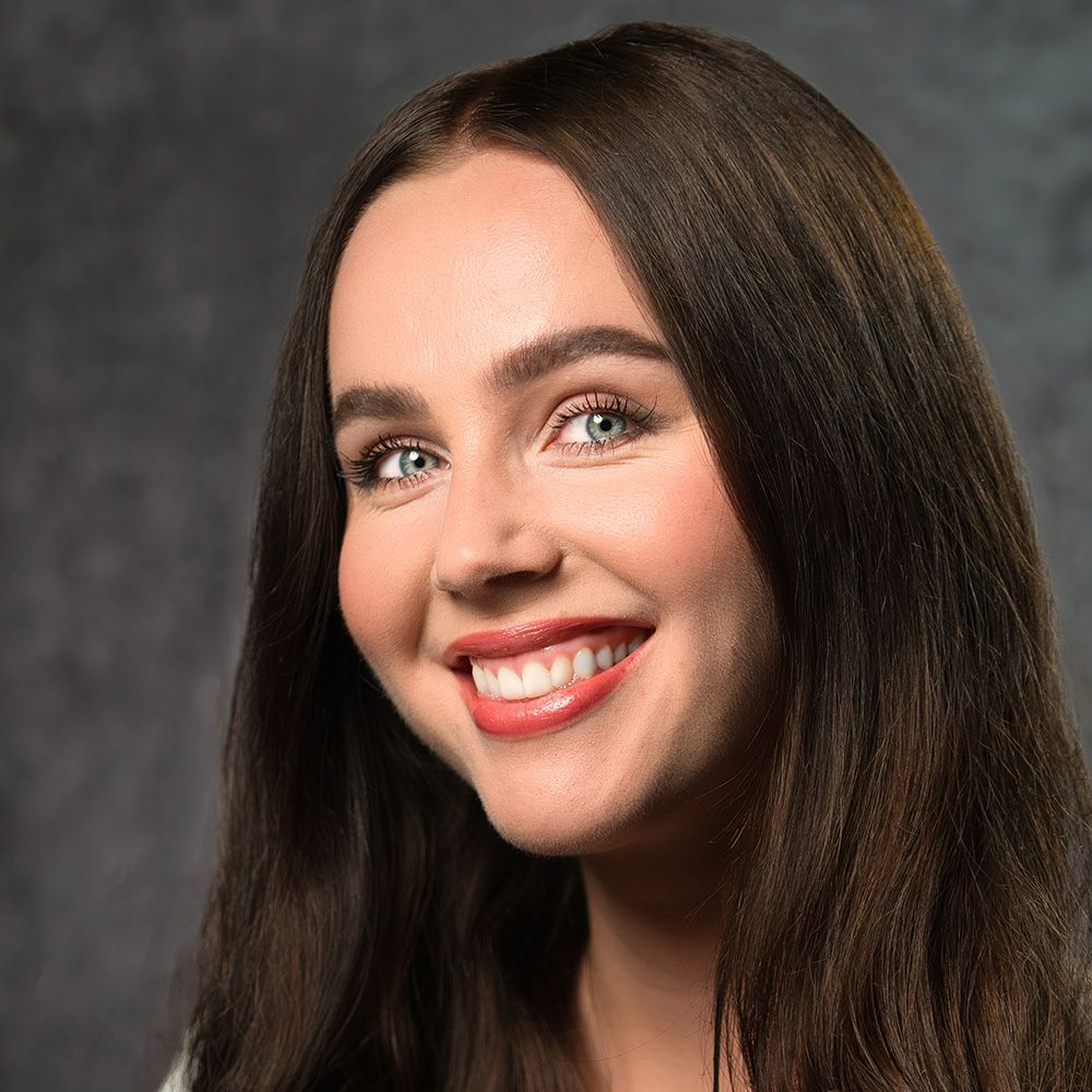 A woman with long brown hair and red lipstick is smiling for the camera.