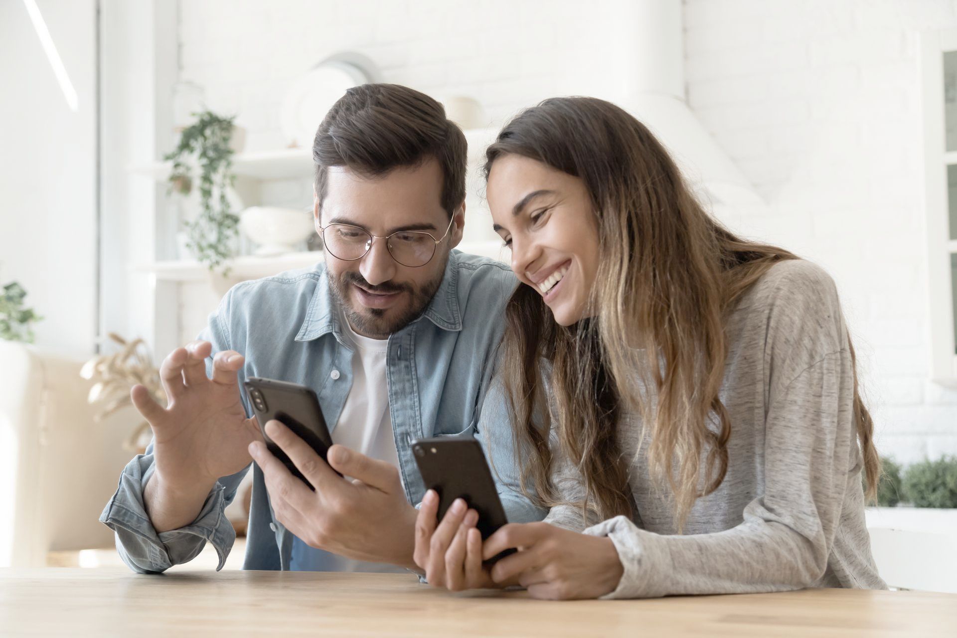 A man and a woman are sitting at a table looking at their phones.