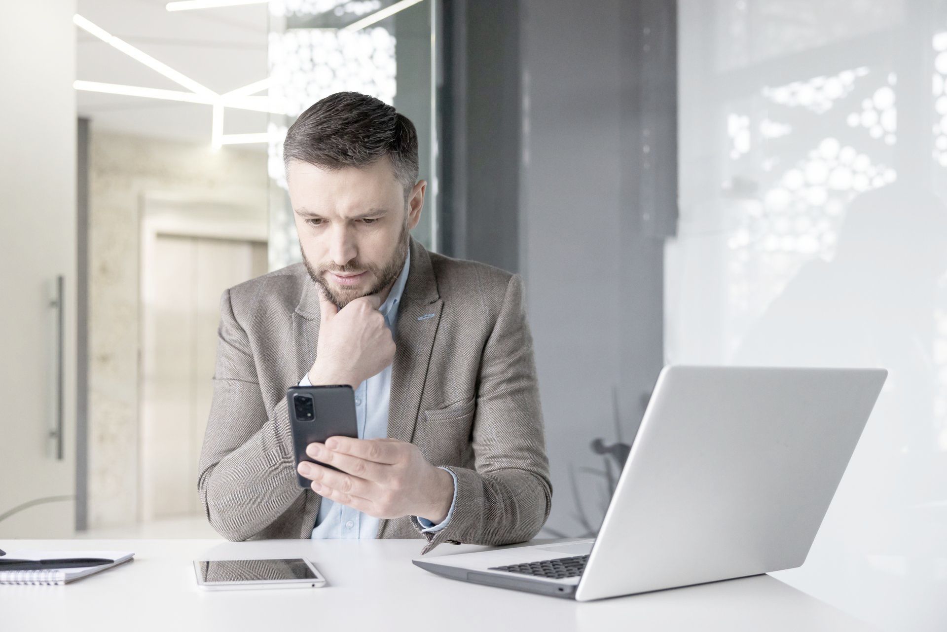 A man is sitting at a desk looking at his cell phone.