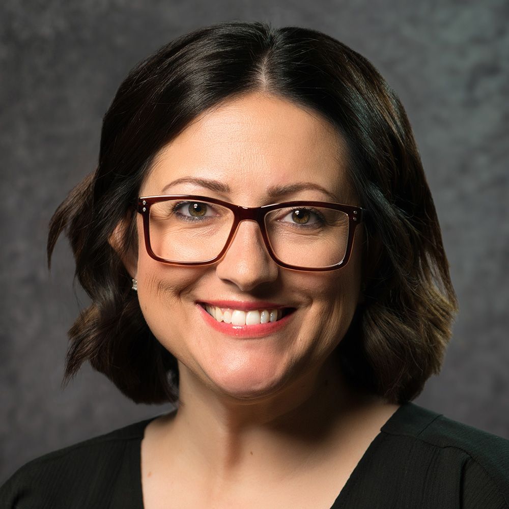 A woman wearing glasses and a black shirt is smiling.