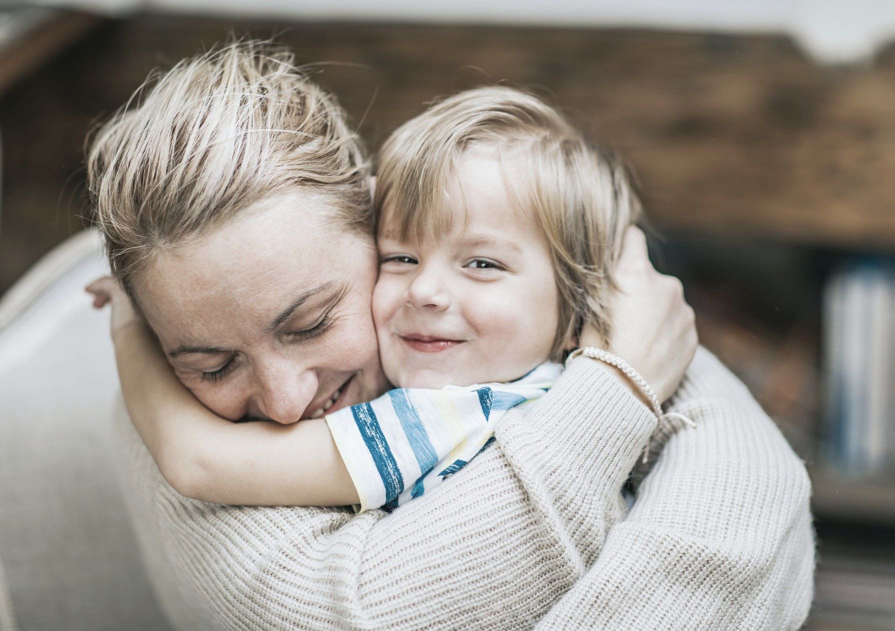 A woman is hugging a little boy who is smiling.