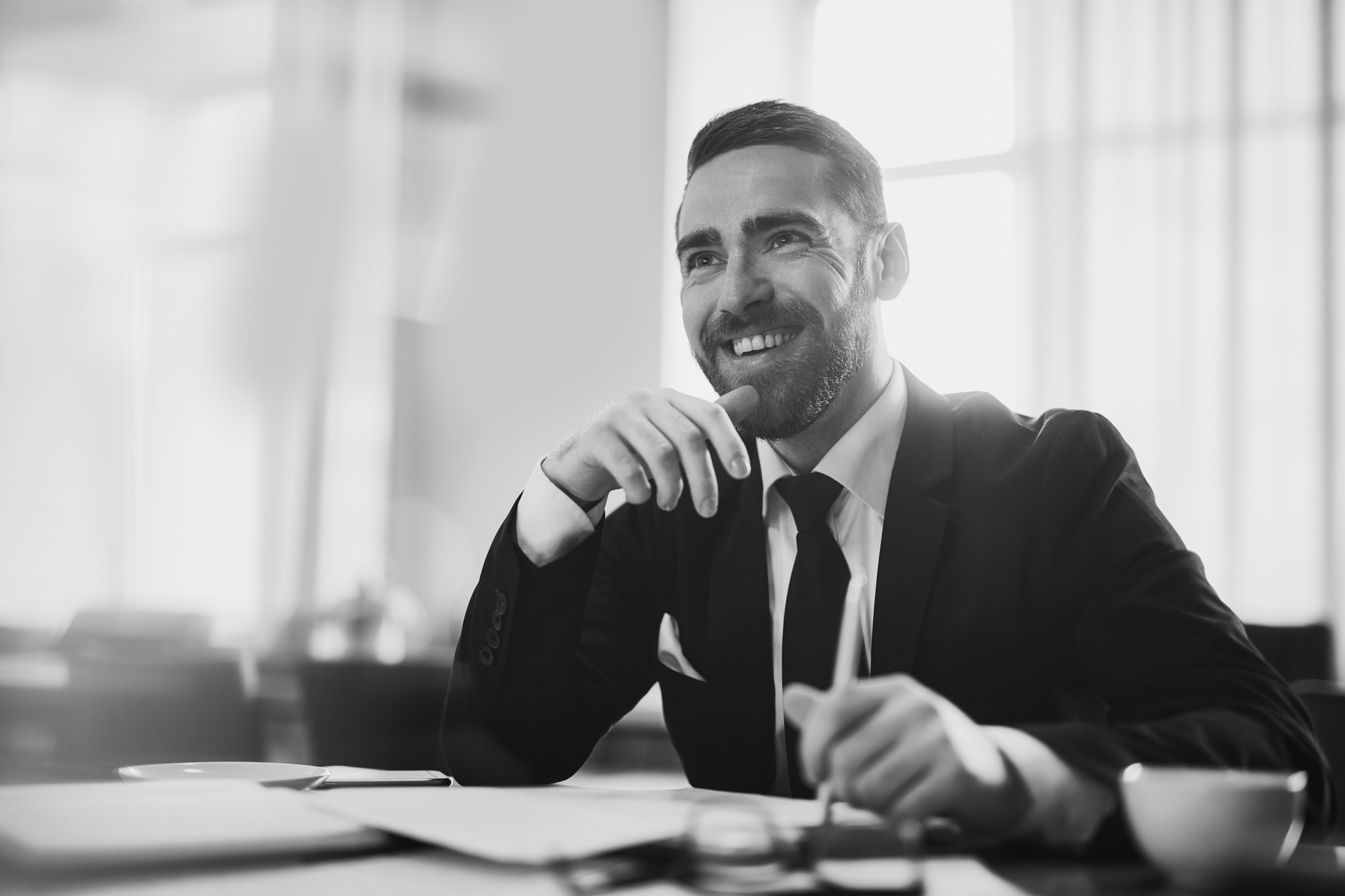 A black and white photo of a man in a suit and tie sitting at a desk.