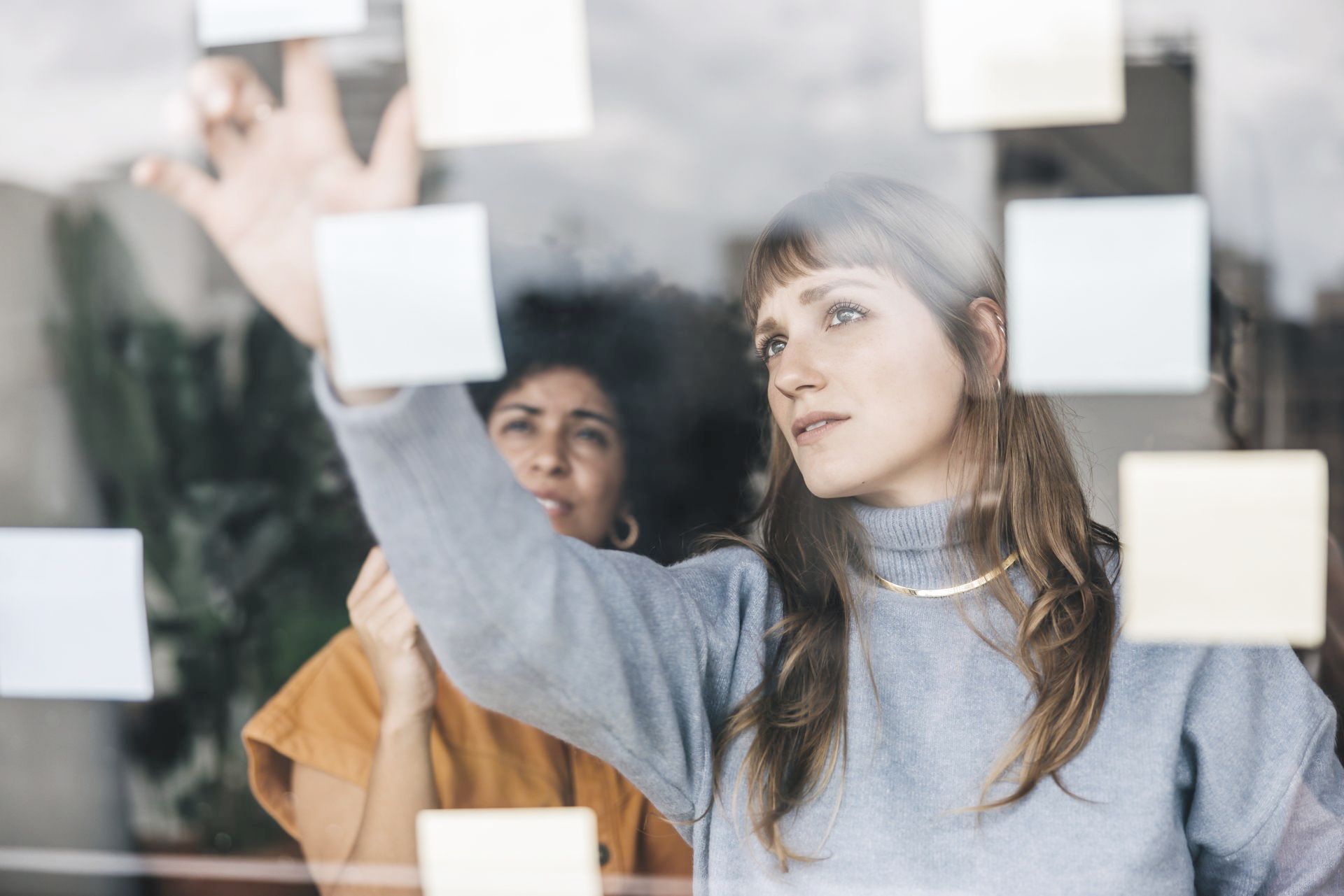 Two women are looking at sticky notes on a window.