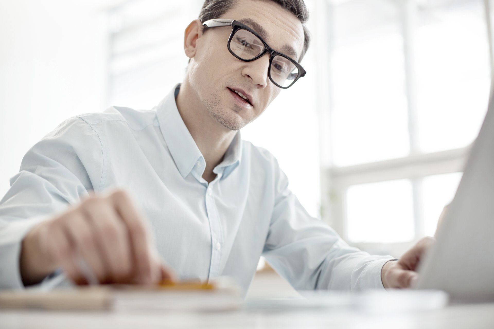 A man wearing glasses is sitting at a desk using a laptop computer.