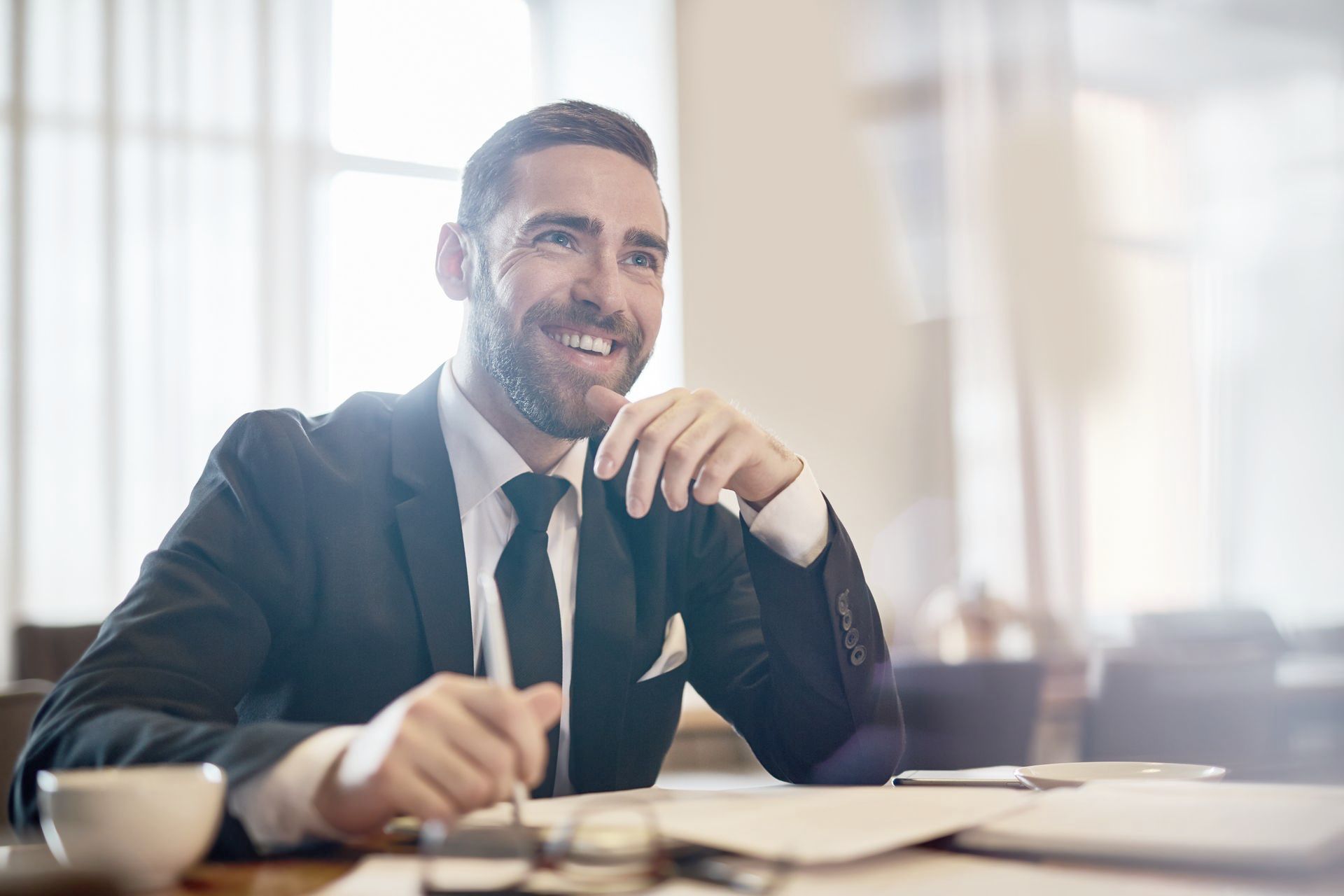 A man in a suit and tie is sitting at a table with a cup of coffee.