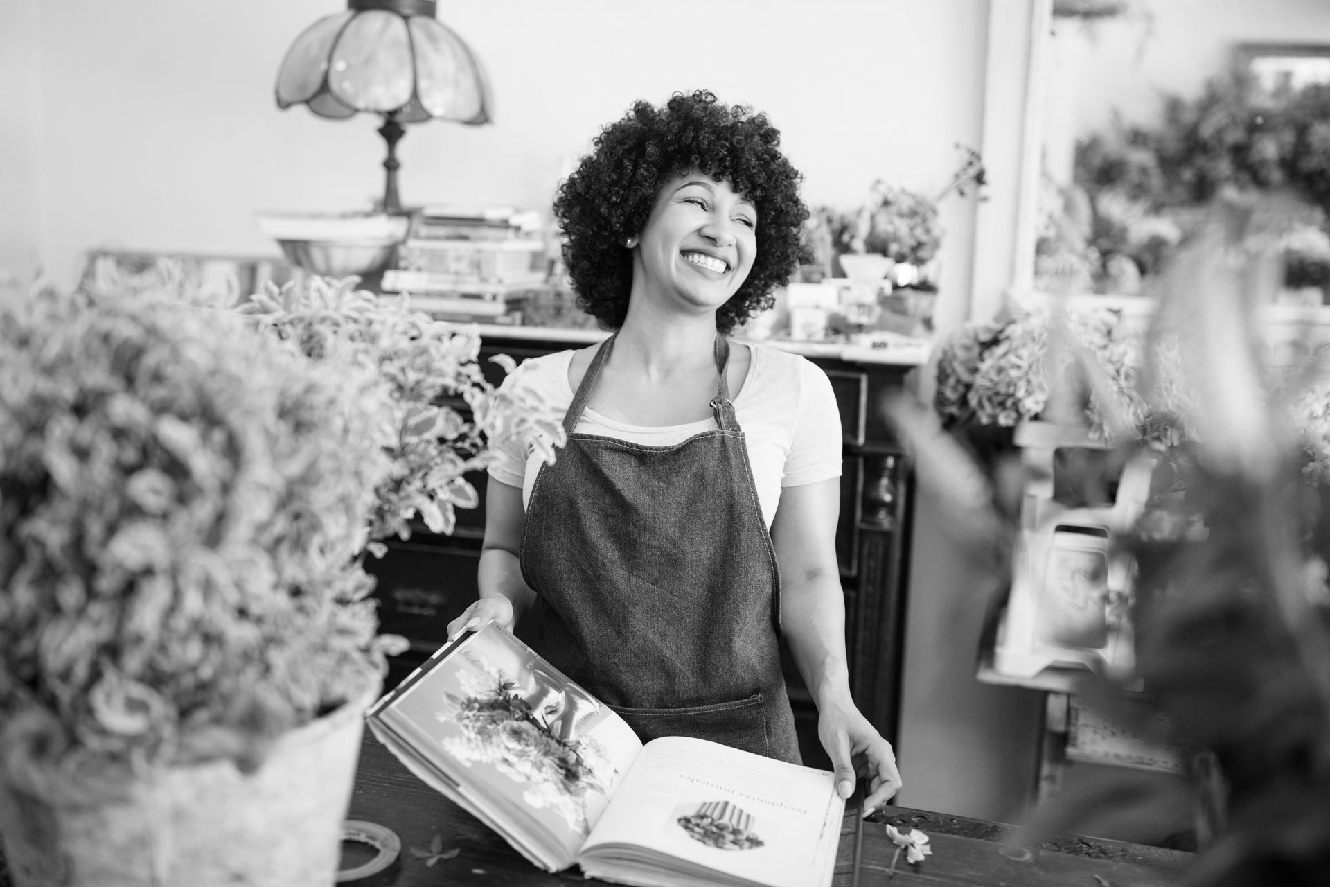 A woman is smiling while holding a book in a black and white photo.