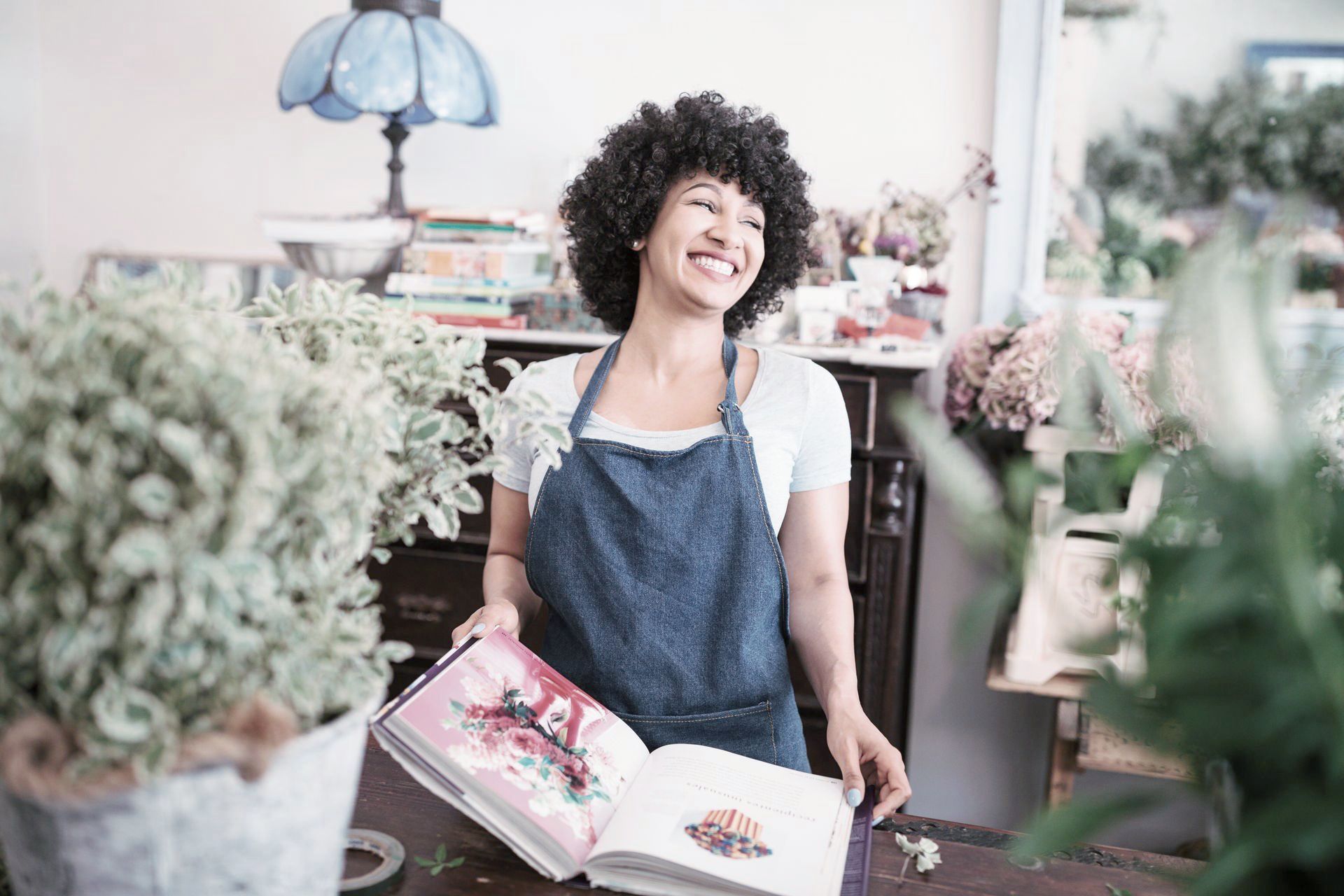 A woman in an apron is holding a book in a flower shop.