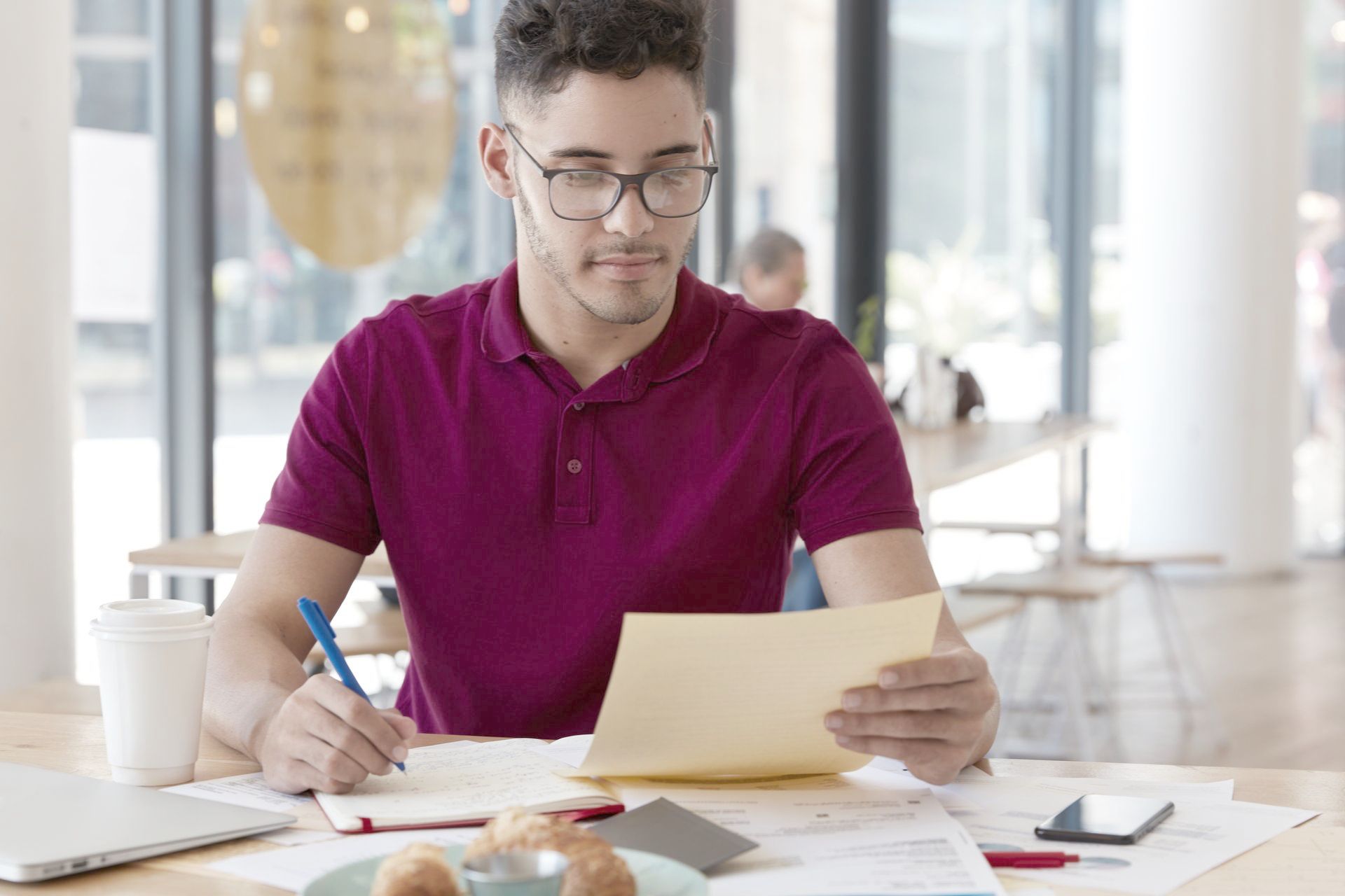 A man is sitting at a table reading and writing on a piece of paper.