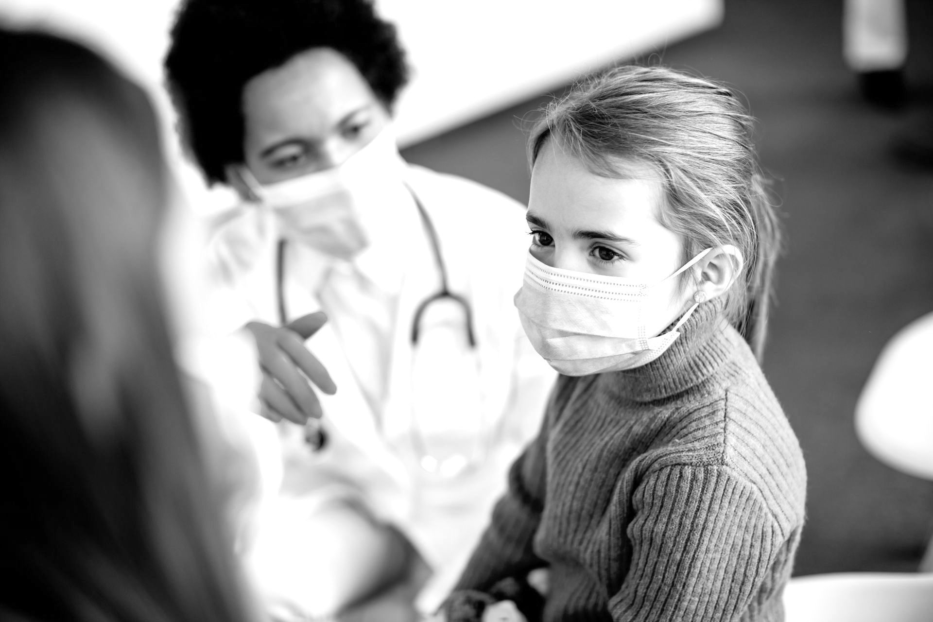 a little girl wearing a mask talks to a doctor