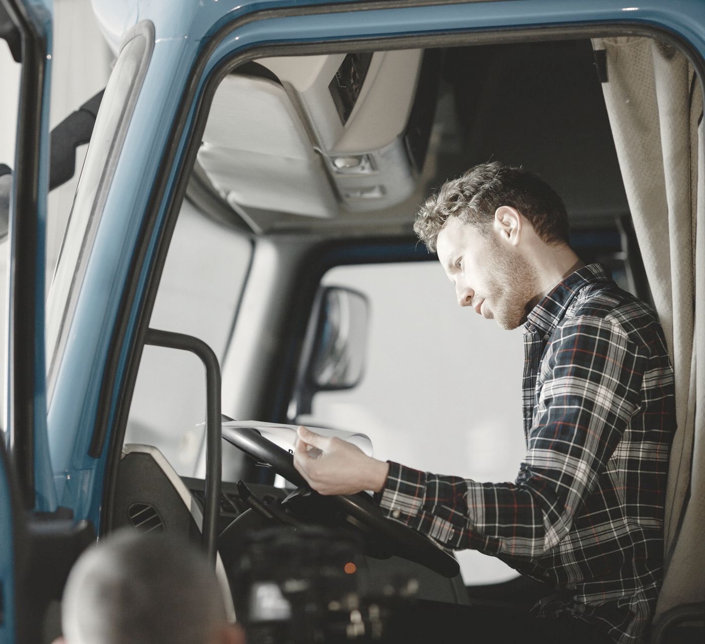 A truck driver sits in his cab looking at paperwork