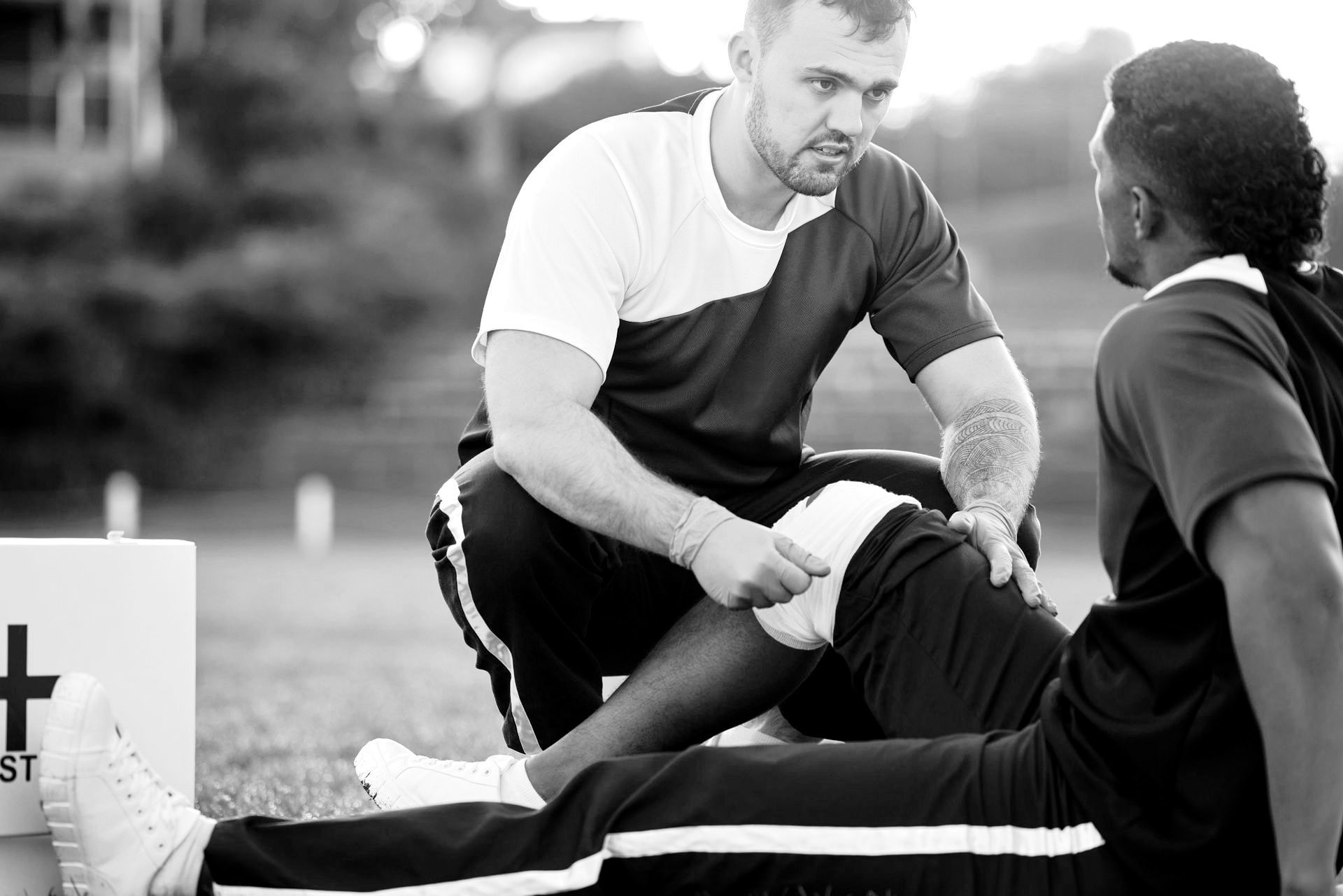 a black and white photo of a man helping another man with his knee