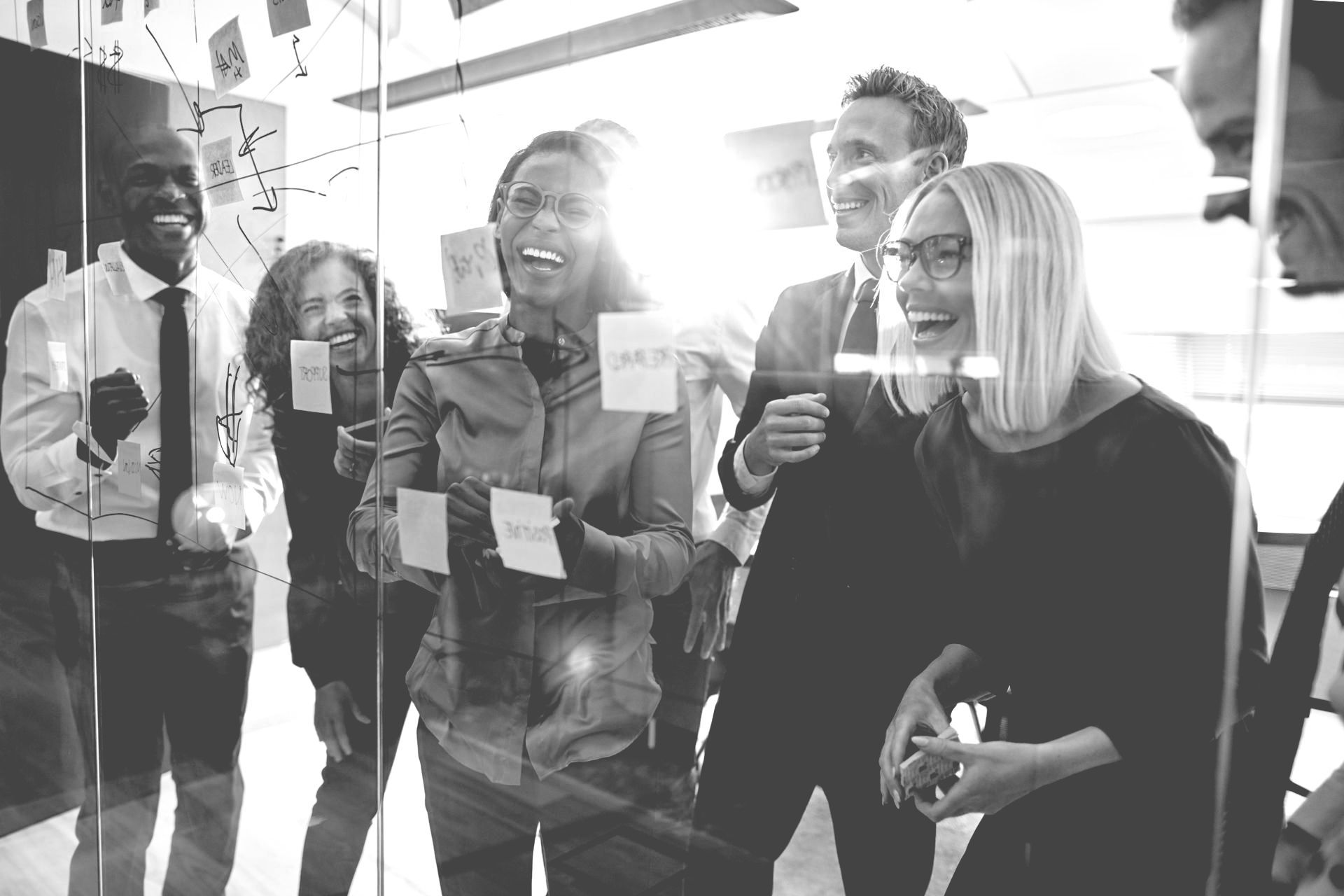 A group of people are standing in front of a glass wall holding sticky notes.